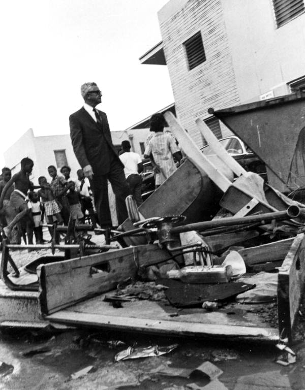 Former Governor Collins stands on top of a pile of objects with Black kids in the background
